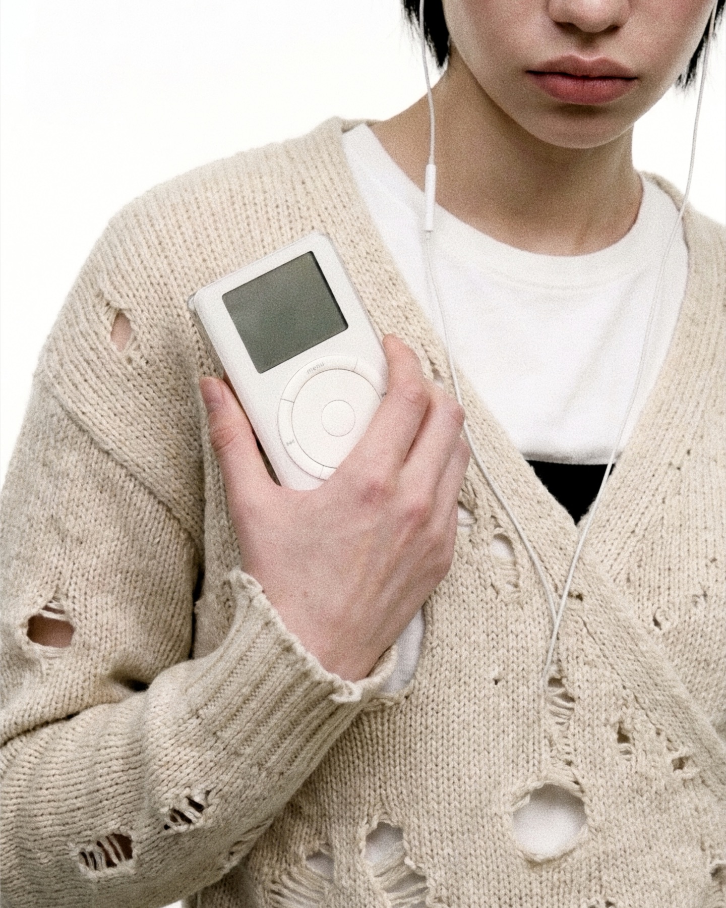 Museum of Tech — a distressed cardigan, a hand holding a classic click-wheel iPod, wired earbuds still in